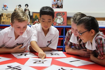 Four children in classroom looking at Asian characters on laminated A4 paper