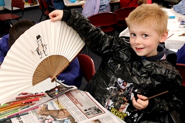 A young boy decorates a paper fan with his own painting