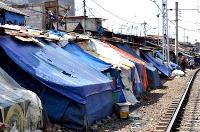Homes with plastic tarpaulins as roofs, next to the train tracks
